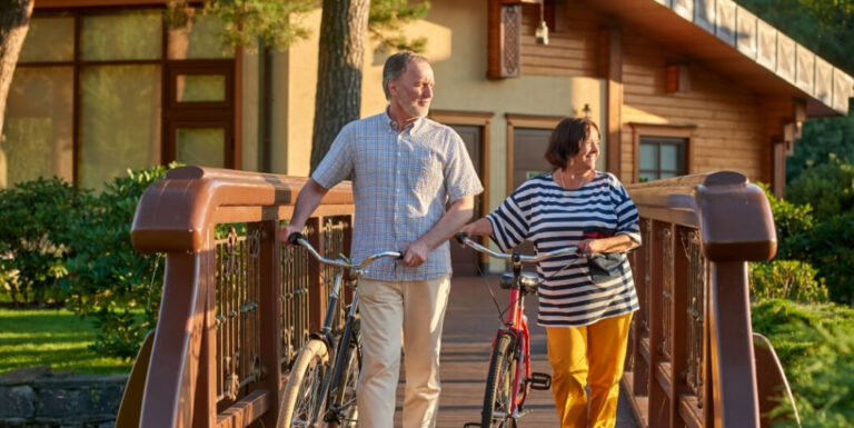 Elderly Couple Walking Bicycles near Cottage at Independent Living Facility